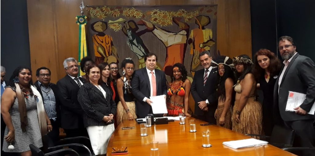 Foto retrata quinze pessoas em pé. Ao centro, uma delas segura um documento. Da esquerda para a direita estão Rutian Pataxó (integrante da Associação Nacional de Ação Indigenista), Gersem Baniwa (integrante do Fórum Nacional de Educação Escolar Indígena), Bacelar (deputado do PODE), Benilda Brito (integrante da Articulação de Organizações de Mulheres Negras do Brasil), Rosa Neide (deputada do PT), Dorinha (deputada do DEM), Ana Ferreira (integrante da Associação Nacional de Ação Indigenista), Joana Tuxá (estudante indígena), Rodrigo Maia (deputado do DEM), Shayres Pataxó (estudante indígena), Daniel Almeida (deputado do PCdoB), Clarice Pataxó (estudante indígena), Simeia Tupinambá (estudante indígena), Denise Carreira (coordenadora da Ação Educativa) e Daniel Cara (coordenador da Campanha Nacional pelo Direito à Educação). Foto retrata momento após Shayres entregar carta da nobel da paz, Malala Yousafzai a Rodrigo Maia.